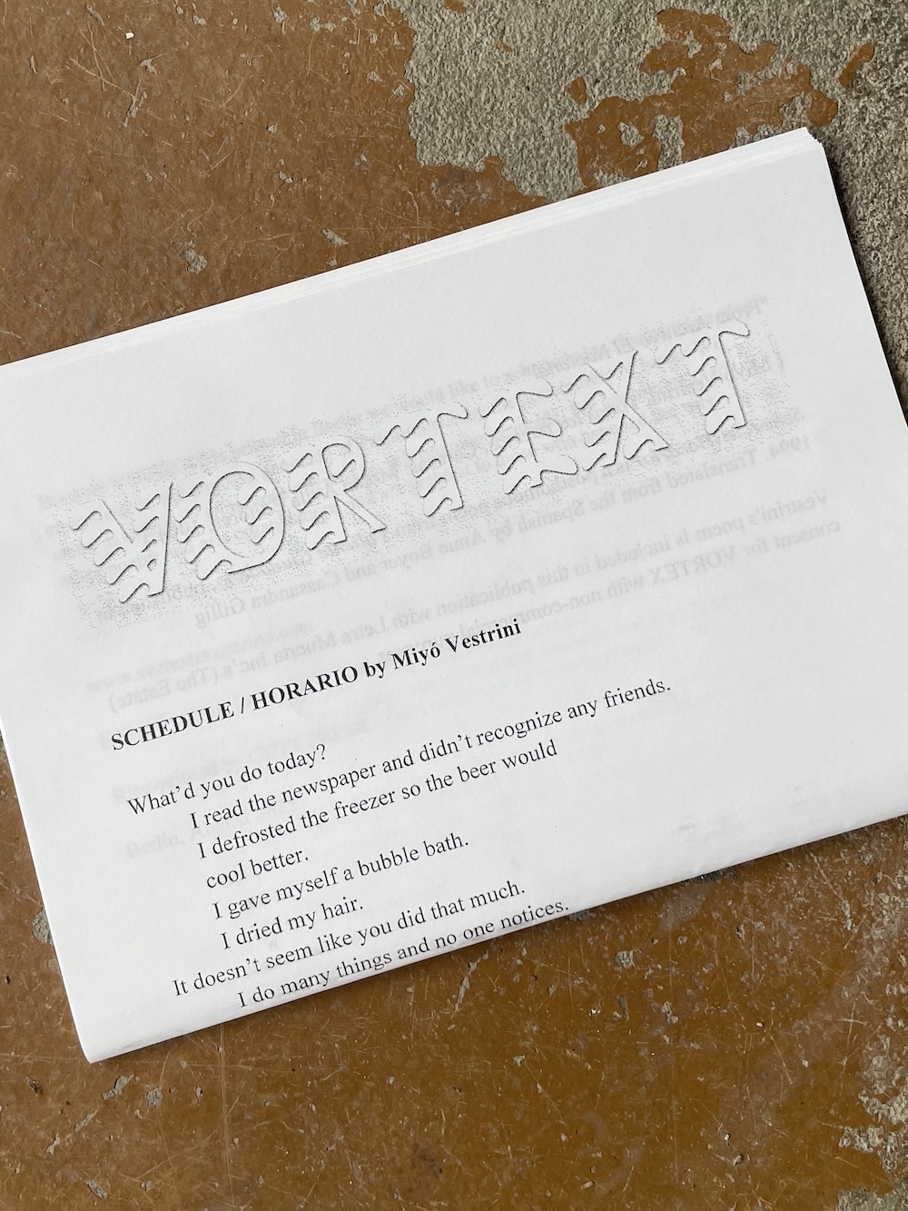 A photograph of the third issue of VORTEXT, folded in half, with the title poem 'Schedule / Horario' by Miyó Vestrini partly visible.